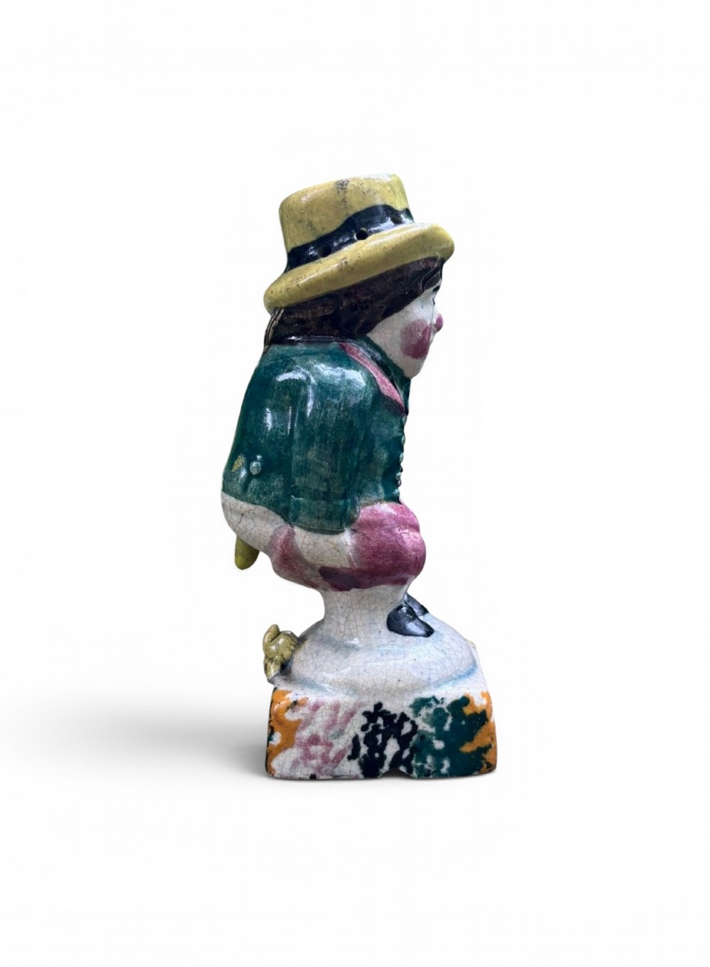 An antique ceramic Prattware figural pepper pot depicting a male character in a yellow top hat, green coat, and pink trousers on a square base. View VIII