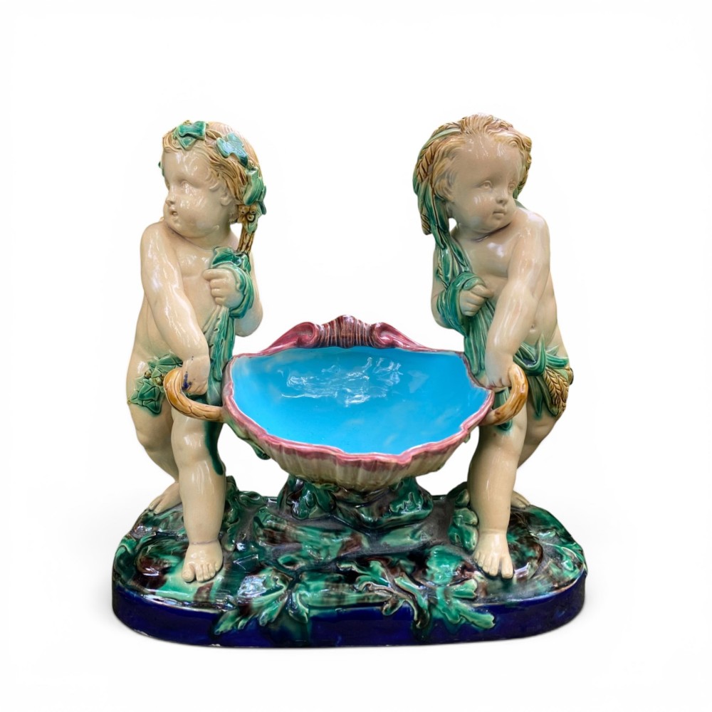A Victorian Minton majolica centrepiece featuring two cherub figures supporting a shell-shaped bowl with a bright turquoise interior on a green foliate base.