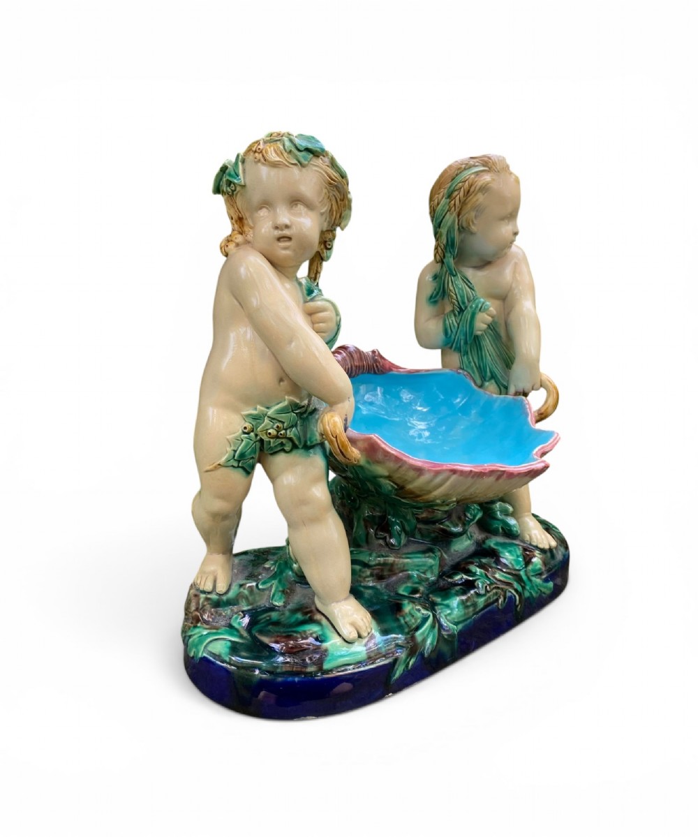 A Victorian Minton majolica centrepiece featuring two cherub figures supporting a shell-shaped bowl with a bright turquoise interior on a green foliate base. View II