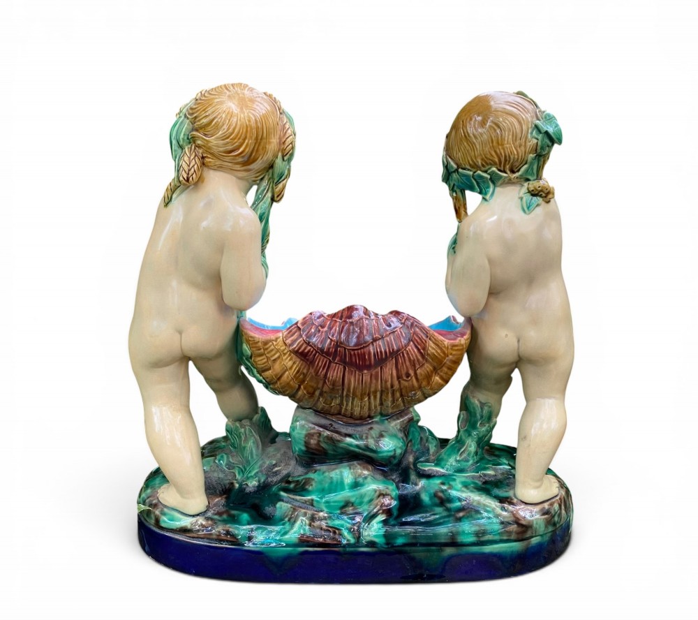 A Victorian Minton majolica centrepiece featuring two cherub figures supporting a shell-shaped bowl with a bright turquoise interior on a green foliate base. View IV