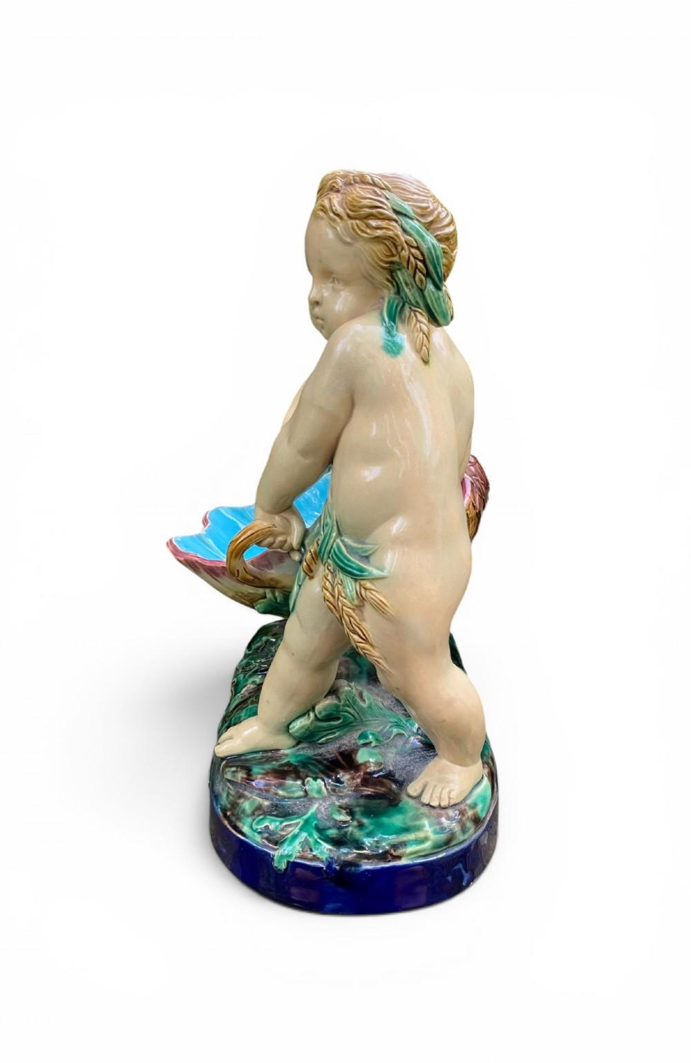 A Victorian Minton majolica centrepiece featuring two cherub figures supporting a shell-shaped bowl with a bright turquoise interior on a green foliate base. View V