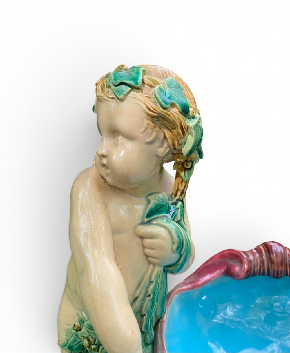 A Victorian Minton majolica centrepiece featuring two cherub figures supporting a shell-shaped bowl with a bright turquoise interior on a green foliate base. View VII