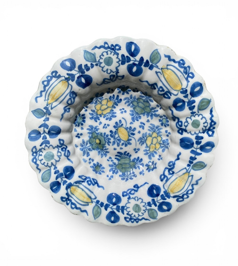 A circular antique Dutch Delft tin-glazed earthenware charger featuring hand-painted polychrome floral motifs in blue, yellow, and green across a fluted lobed rim and central basin.