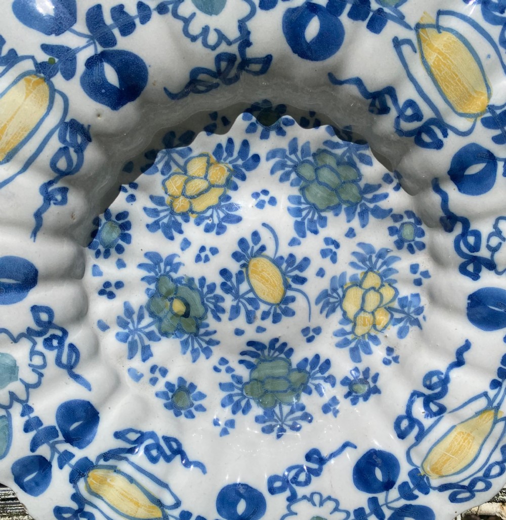 A circular antique Dutch Delft tin-glazed earthenware charger featuring hand-painted polychrome floral motifs in blue, yellow, and green across a fluted lobed rim and central basin. View II