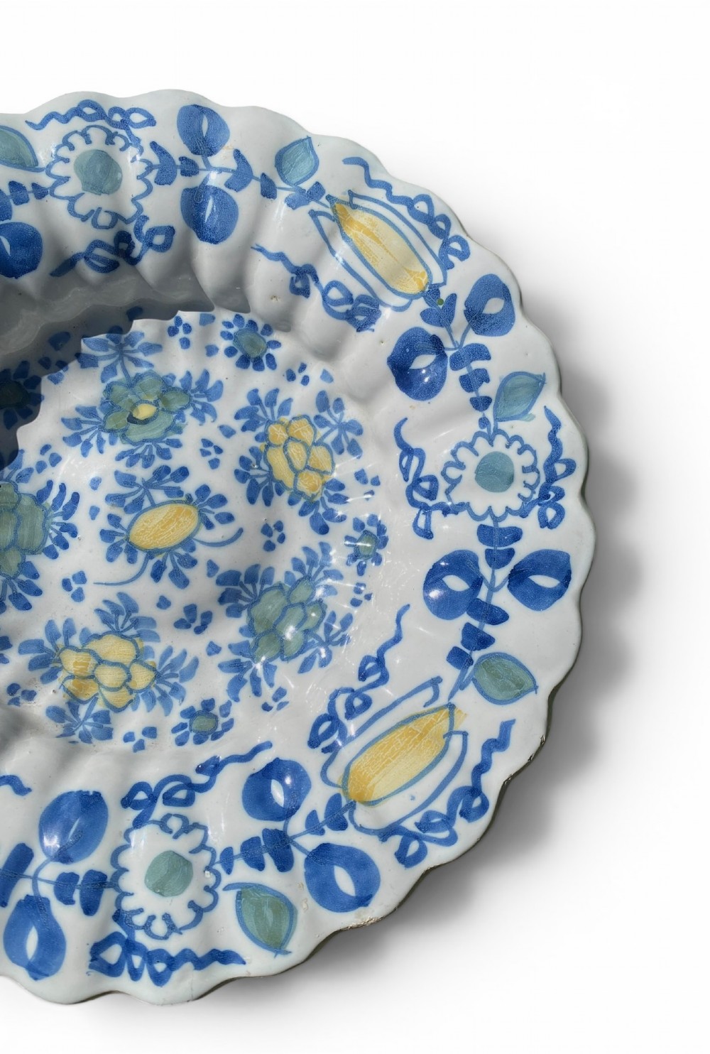 A circular antique Dutch Delft tin-glazed earthenware charger featuring hand-painted polychrome floral motifs in blue, yellow, and green across a fluted lobed rim and central basin. View VI