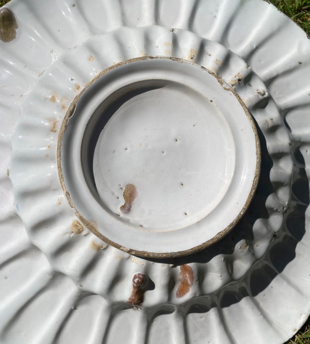 A circular antique Dutch Delft tin-glazed earthenware charger featuring hand-painted polychrome floral motifs in blue, yellow, and green across a fluted lobed rim and central basin. View VII
