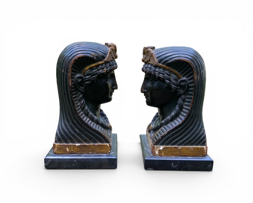 A facing pair of carved dark wood sphinx busts with gilt highlights mounted on rectangular black marble bases.