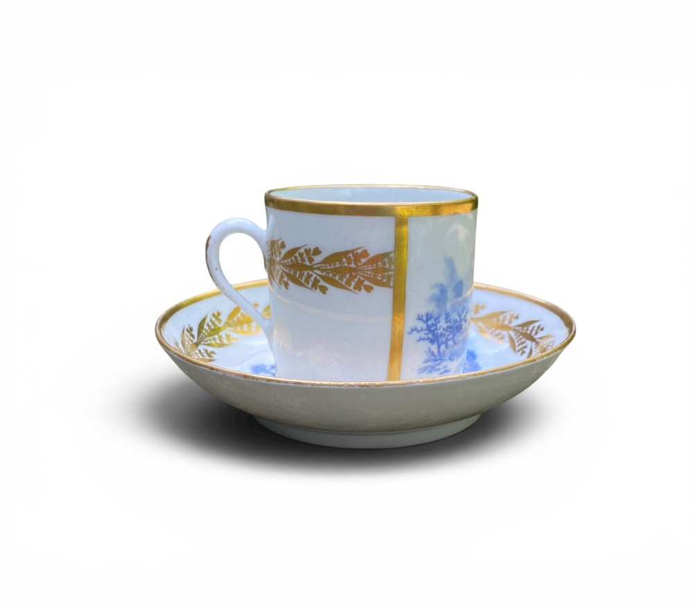 An antique blue and white porcelain coffee can and saucer featuring a painted landscape scene and gilded foliage borders. View III