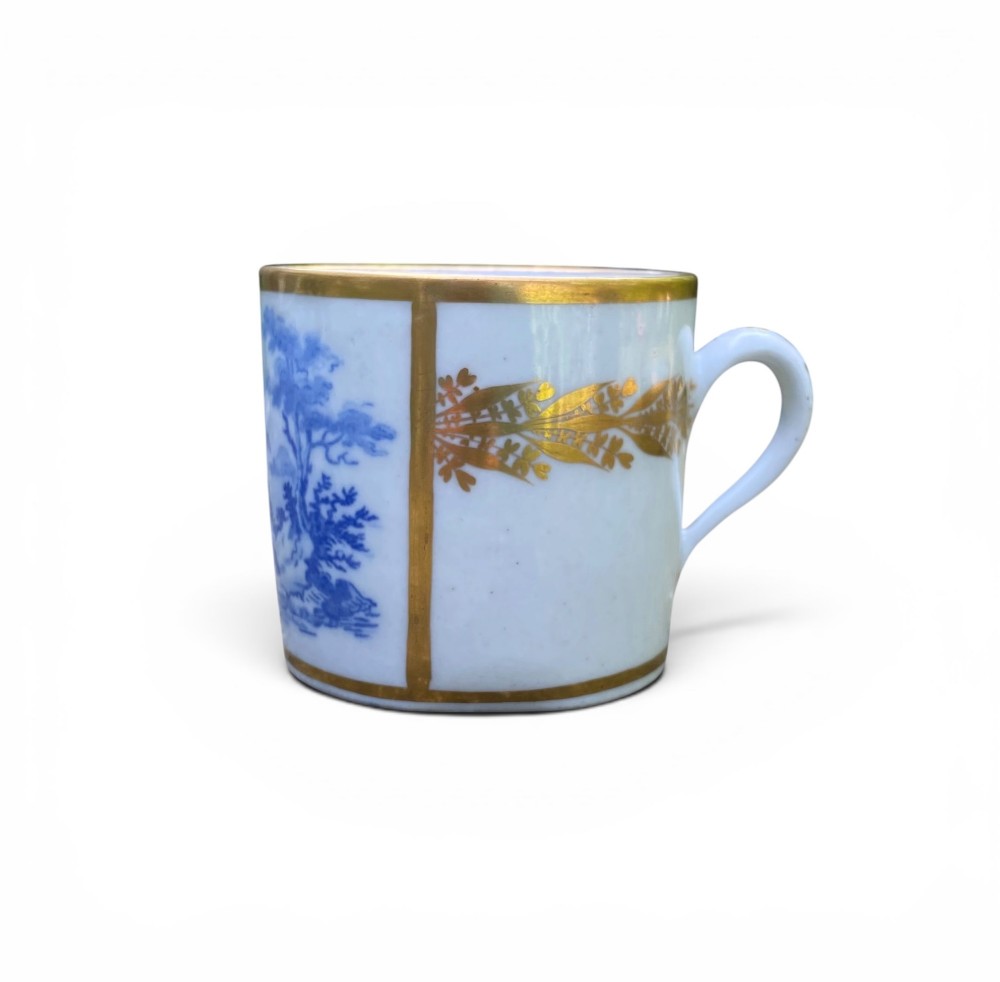 An antique blue and white porcelain coffee can and saucer featuring a painted landscape scene and gilded foliage borders. View IV
