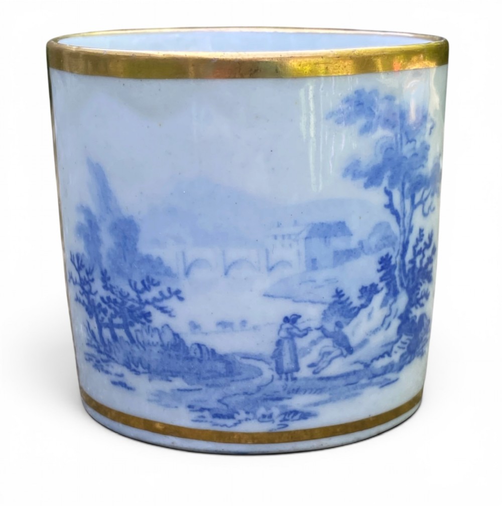 An antique blue and white porcelain coffee can and saucer featuring a painted landscape scene and gilded foliage borders. View V
