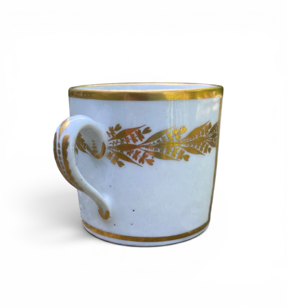 An antique blue and white porcelain coffee can and saucer featuring a painted landscape scene and gilded foliage borders. View VII