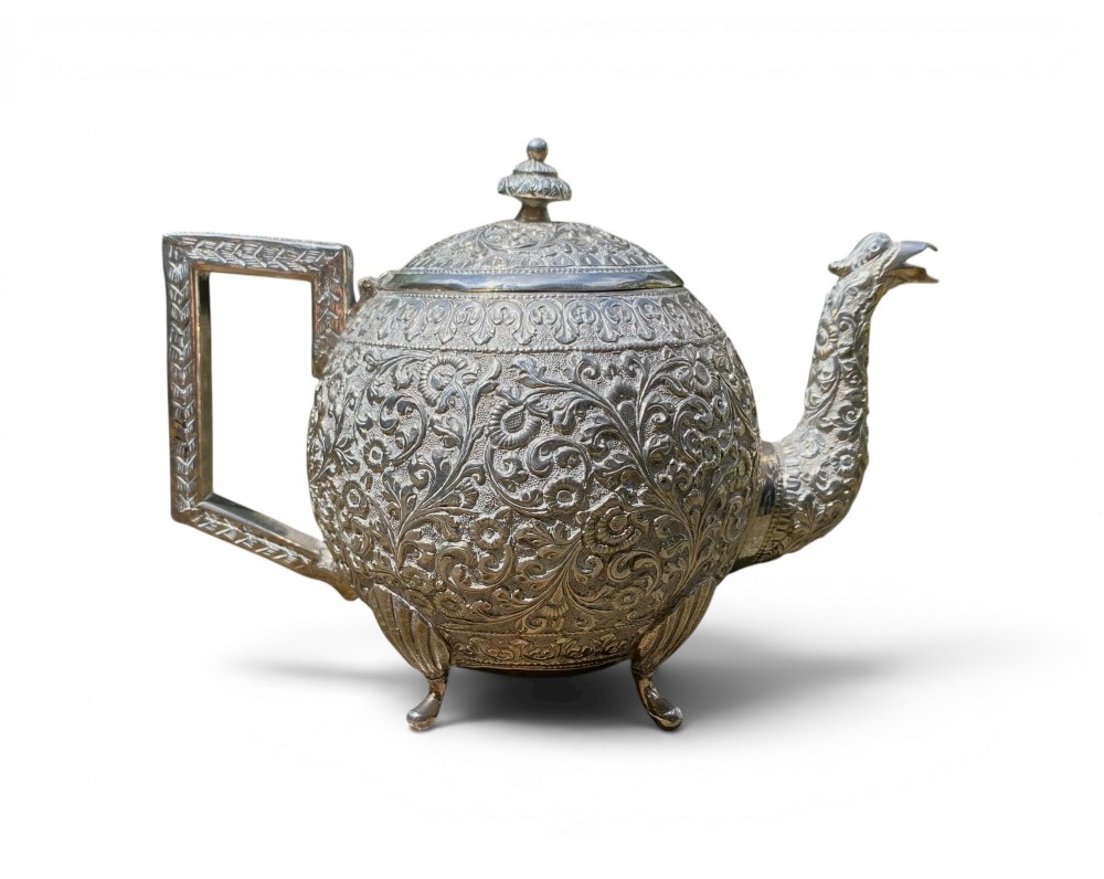 A three-piece antique Indian silver tea service featuring detailed chased floral scrollwork, elephant-shaped lid finials, and angular geometric handles. View II