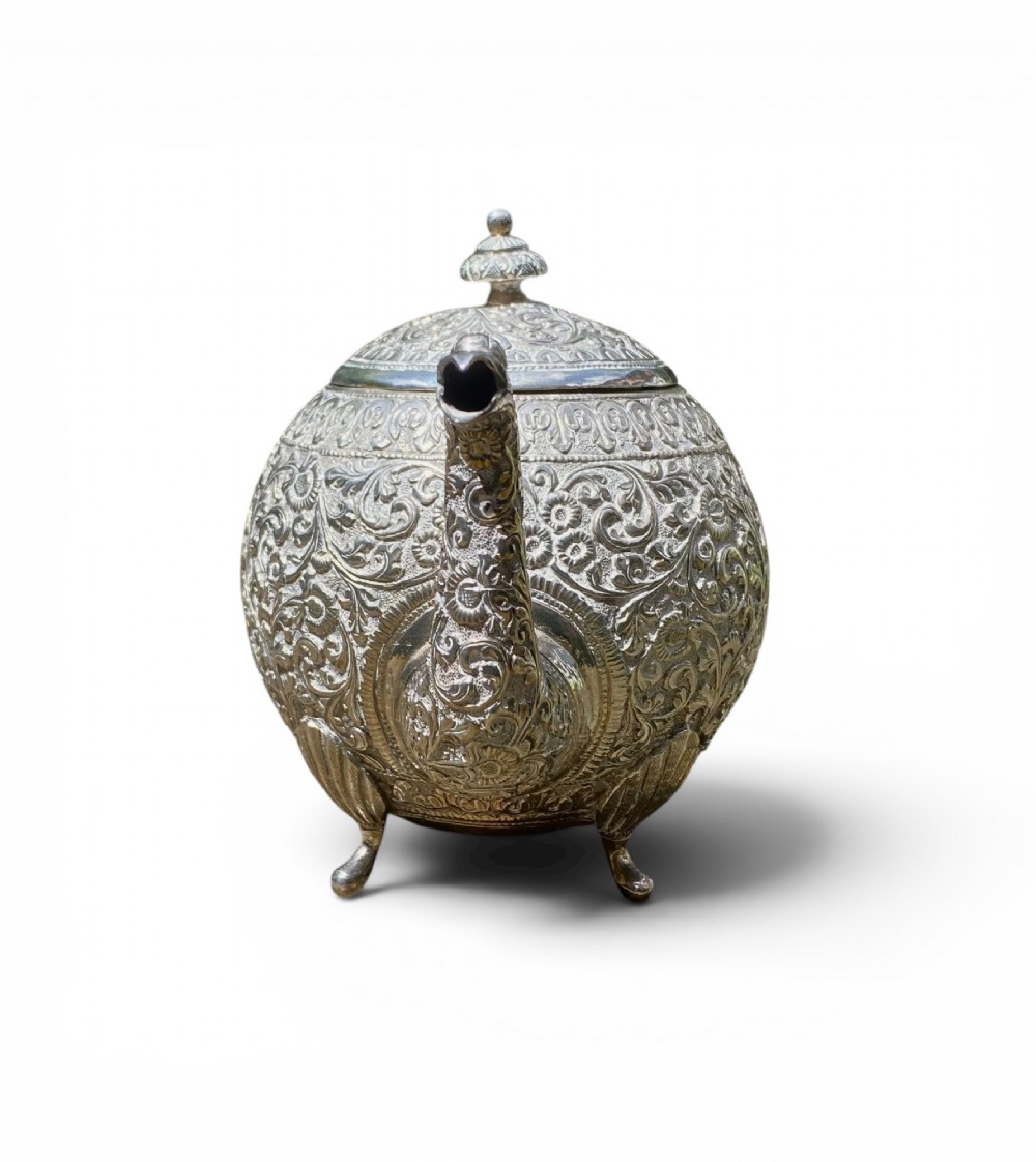 A three-piece antique Indian silver tea service featuring detailed chased floral scrollwork, elephant-shaped lid finials, and angular geometric handles. View III