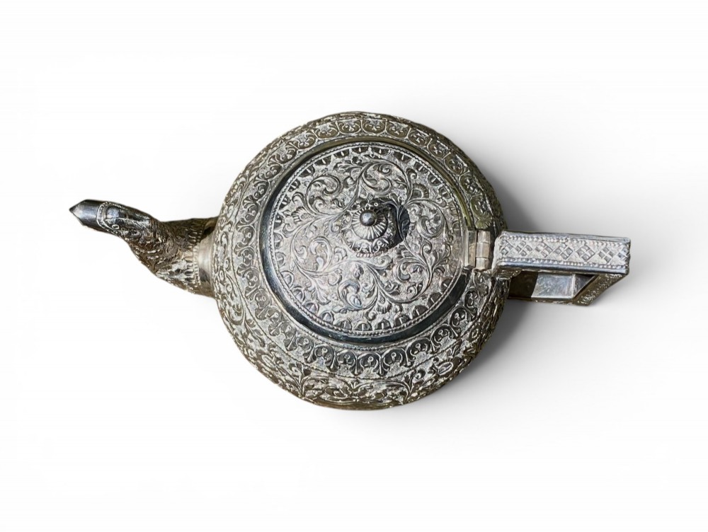 A three-piece antique Indian silver tea service featuring detailed chased floral scrollwork, elephant-shaped lid finials, and angular geometric handles. View VI