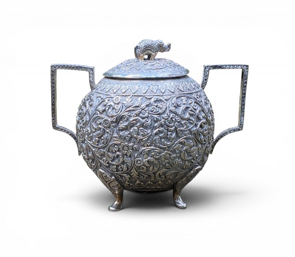 A three-piece antique Indian silver tea service featuring detailed chased floral scrollwork, elephant-shaped lid finials, and angular geometric handles. View VII