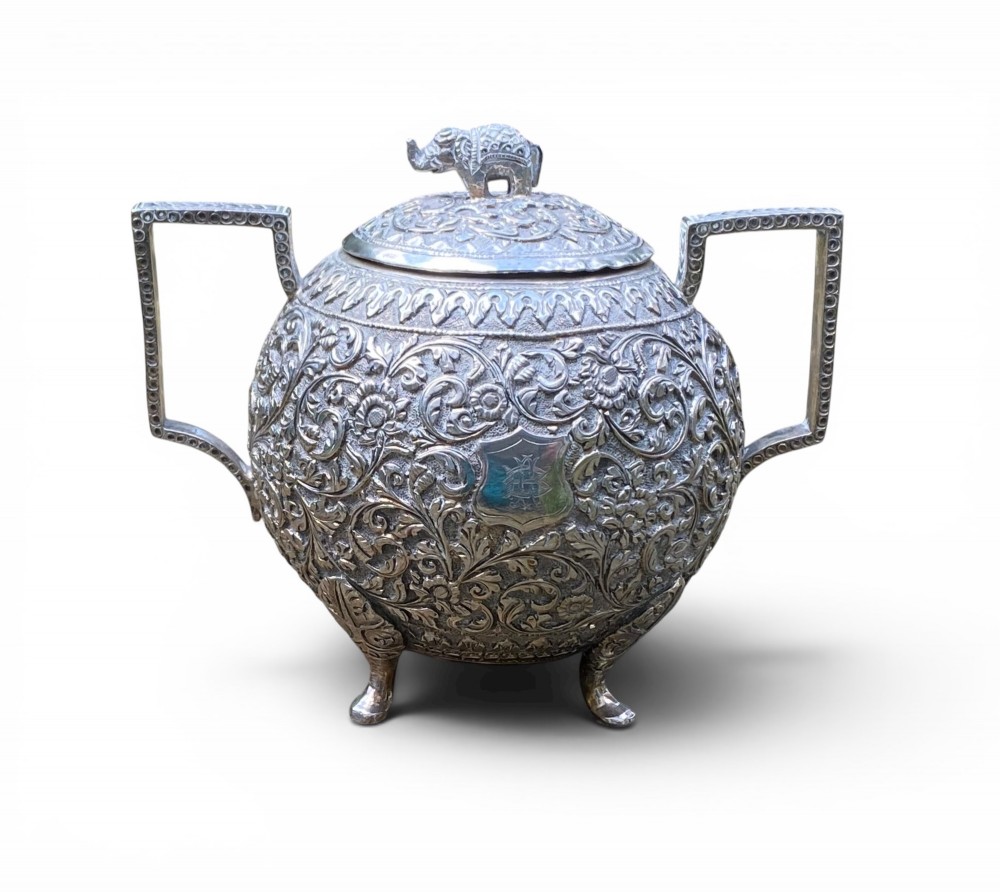 A three-piece antique Indian silver tea service featuring detailed chased floral scrollwork, elephant-shaped lid finials, and angular geometric handles. View VIII