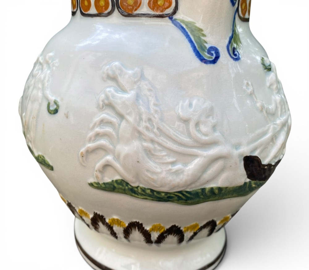 A late 18th-century relief-moulded Prattware ceramic jug featuring polychrome oxide highlights depicting naval battle motifs against an off-white background. View V