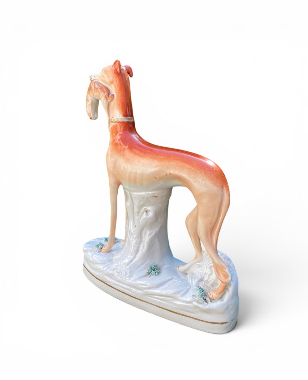 A pair of Victorian Staffordshire earthenware greyhound figurines standing facing each other, each holding a hare in its mouth on a white ceramic base. View XII