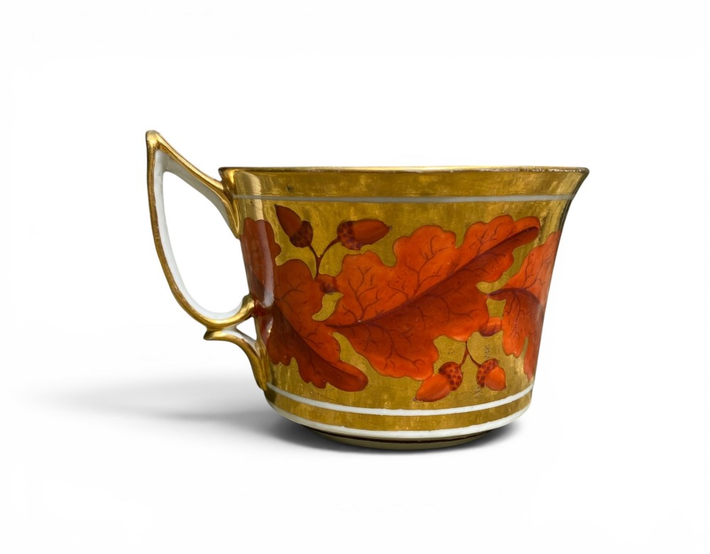 A Regency period Derby porcelain trio featuring two cups and a matching saucer decorated with red oak leaves and heavy gilding. View IX