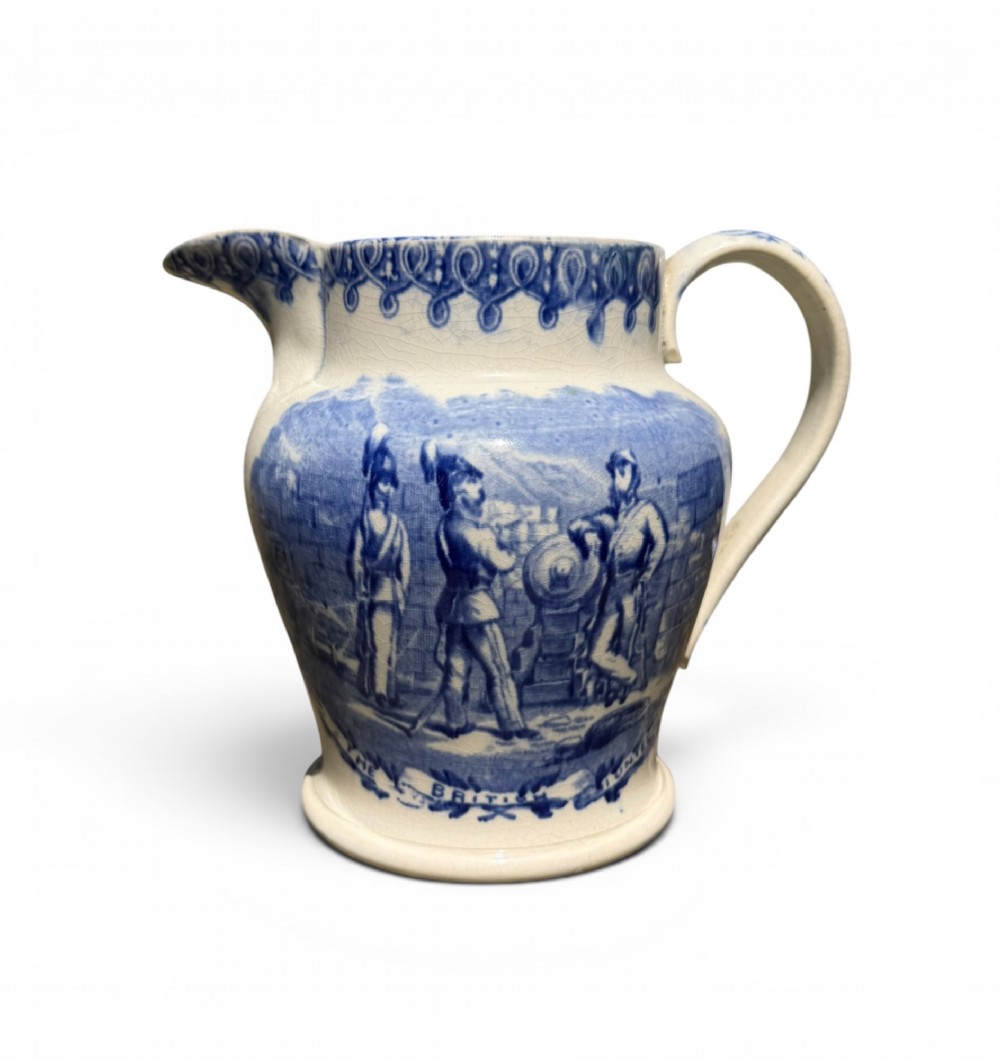 A cream earthenware jug featuring cobalt blue transferware depicting military figures labeled The British Volunteers.