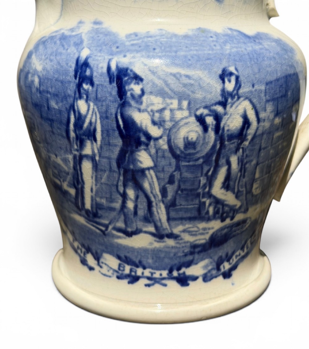 A cream earthenware jug featuring cobalt blue transferware depicting military figures labeled The British Volunteers. View VI