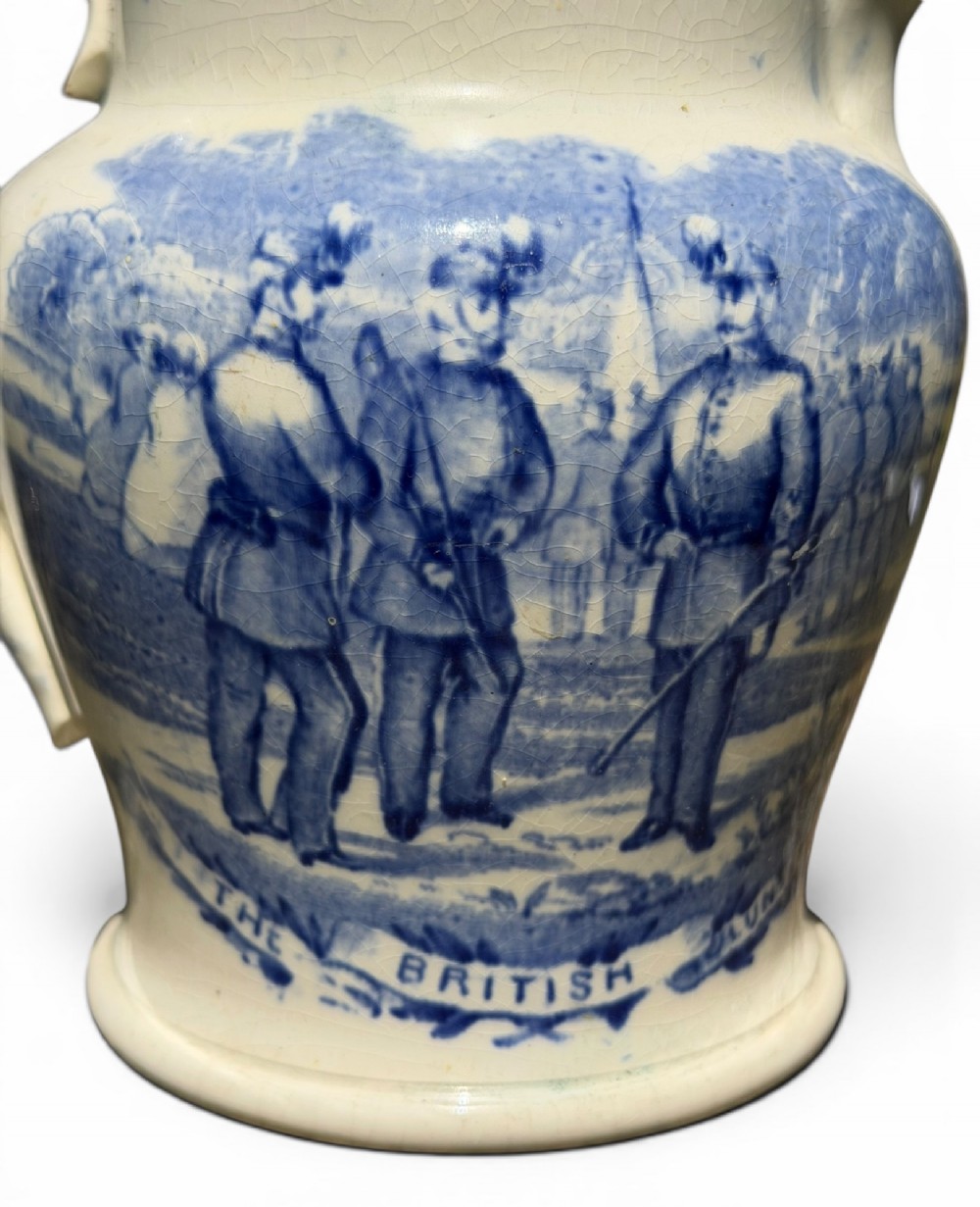 A cream earthenware jug featuring cobalt blue transferware depicting military figures labeled The British Volunteers. View VII