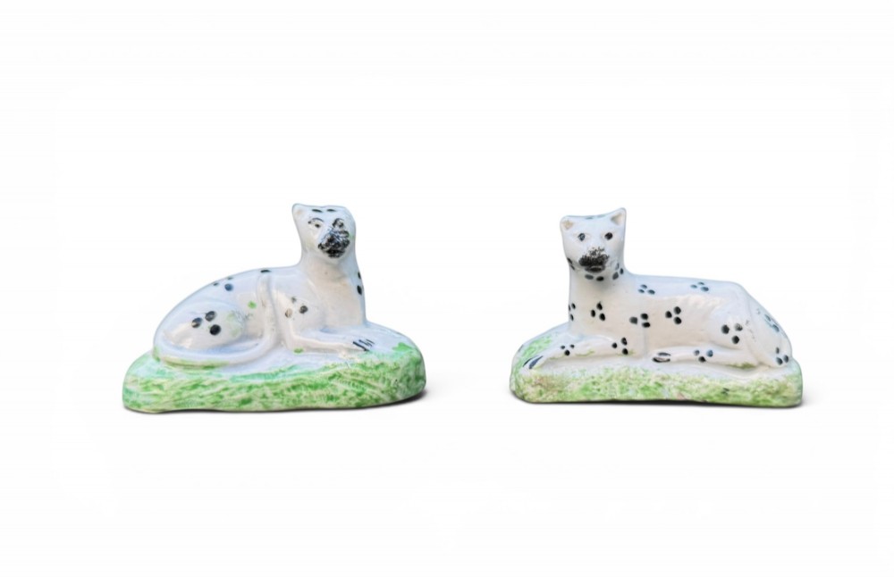 A pair of small antique white pearlware figures of recumbent spotted leopards resting on moulded green bases.
