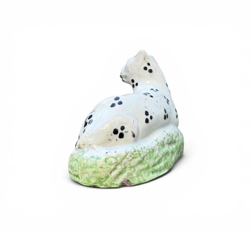 A pair of small antique white pearlware figures of recumbent spotted leopards resting on moulded green bases. View V
