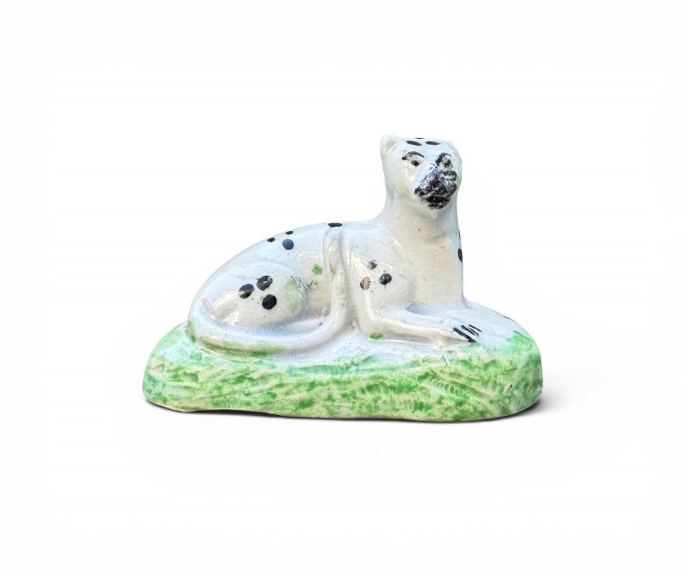 A pair of small antique white pearlware figures of recumbent spotted leopards resting on moulded green bases. View VIII