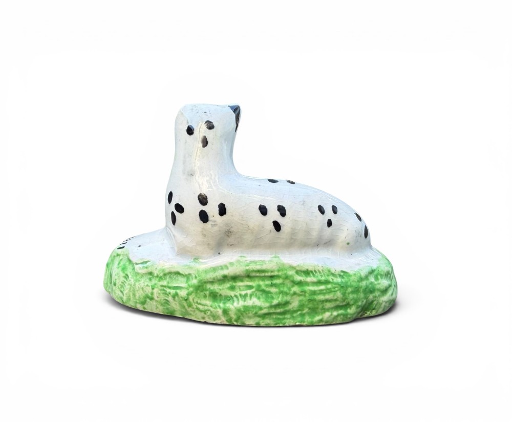 A pair of small antique white pearlware figures of recumbent spotted leopards resting on moulded green bases. View X
