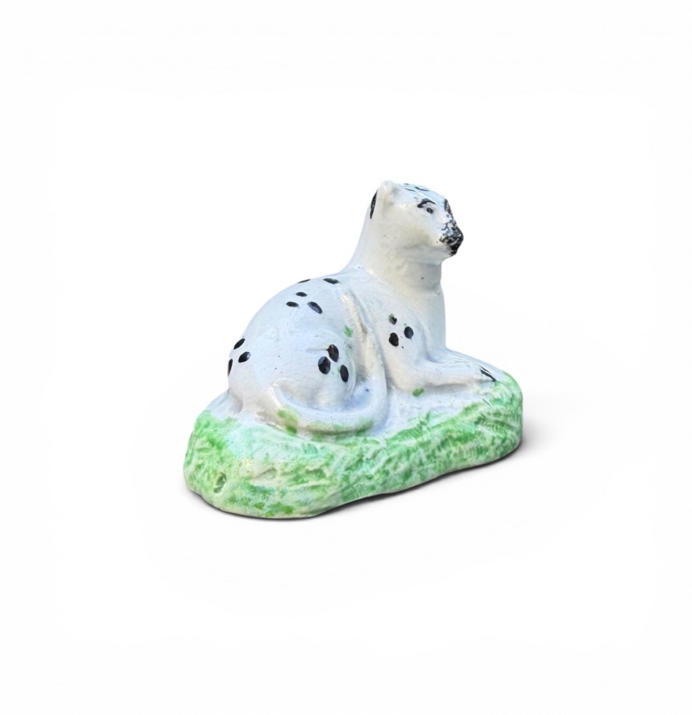 A pair of small antique white pearlware figures of recumbent spotted leopards resting on moulded green bases. View XI