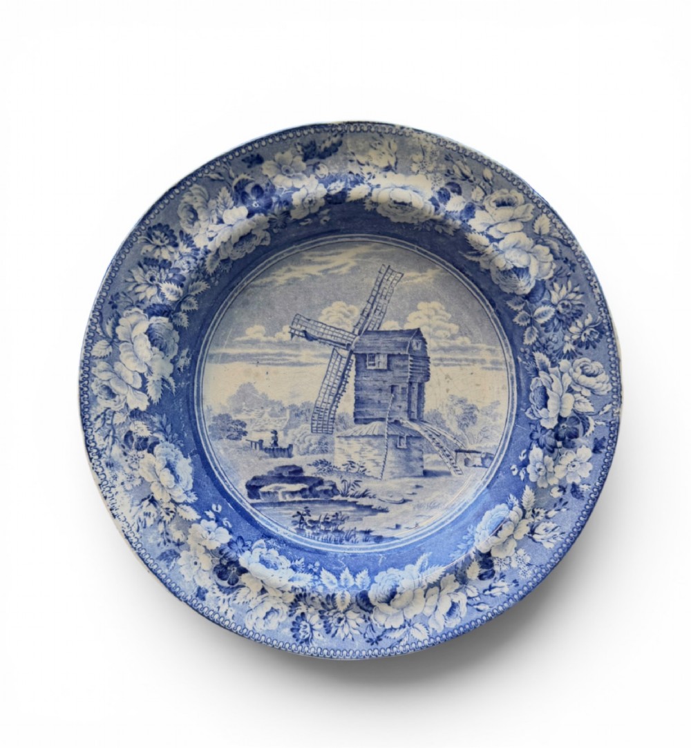 A circular blue and white transferware pottery dish decorated with a central windmill scene and a wide floral border.