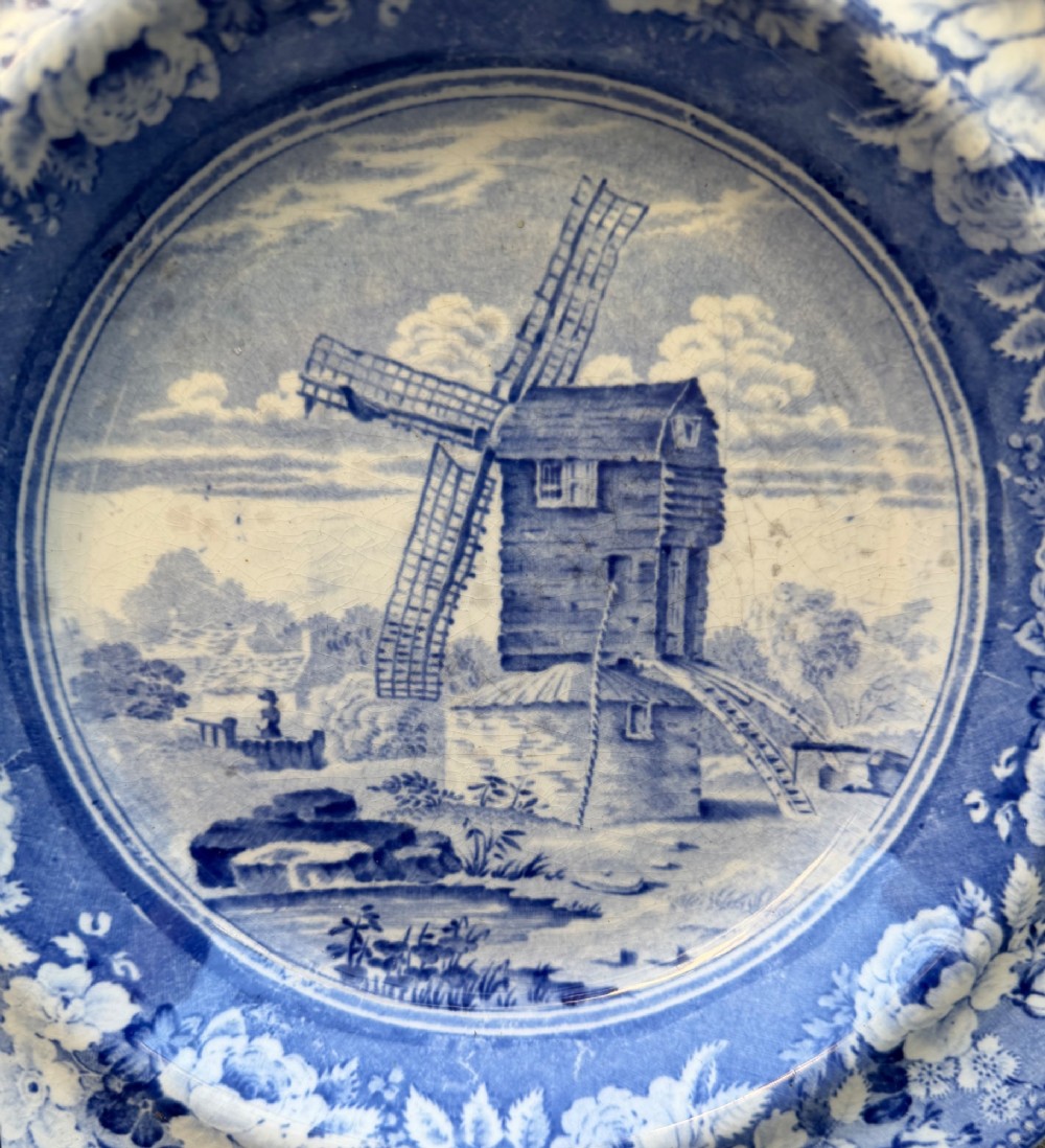 A circular blue and white transferware pottery dish decorated with a central windmill scene and a wide floral border. View II