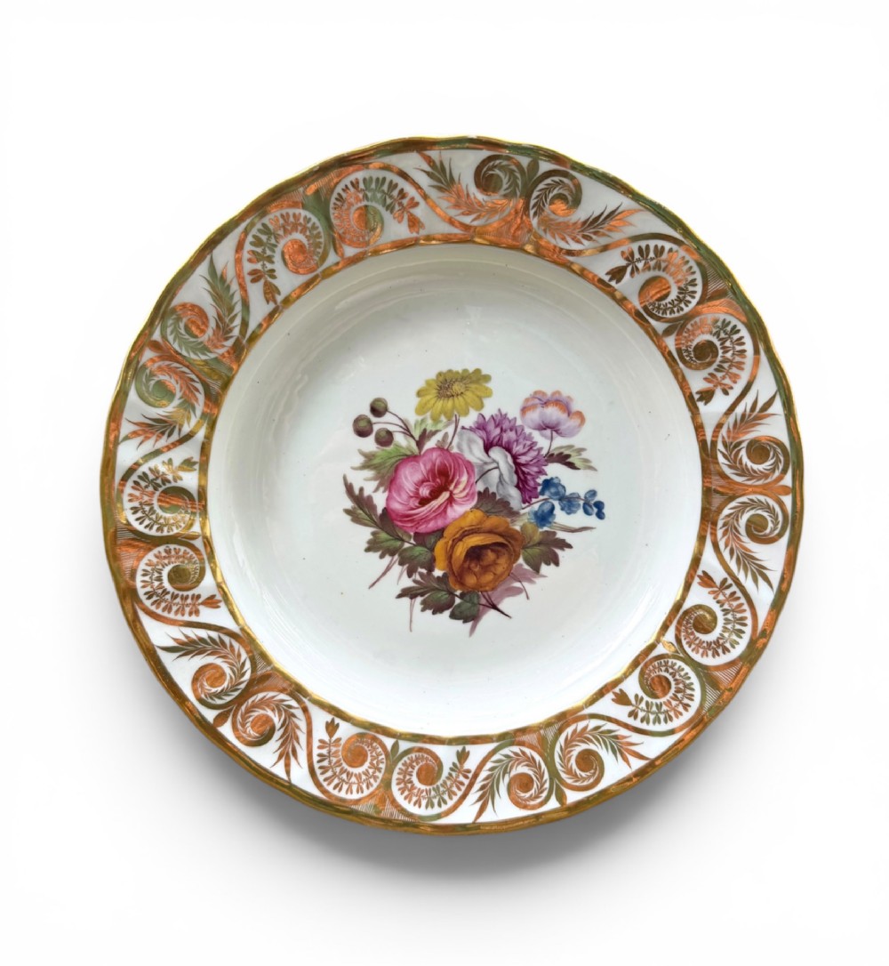 A circular white porcelain dish featuring a hand-painted floral centrepiece framed by a gilded scrollwork rim.