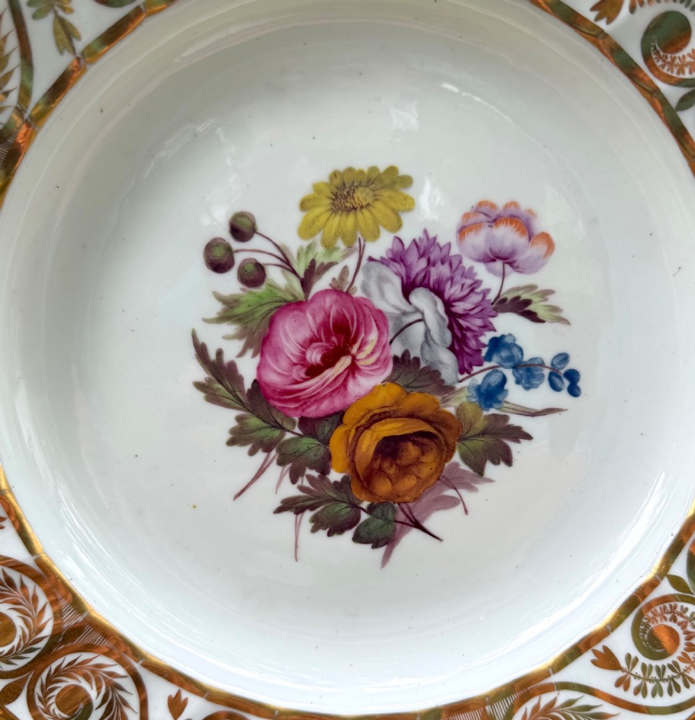 A circular white porcelain dish featuring a hand-painted floral centrepiece framed by a gilded scrollwork rim. View IV