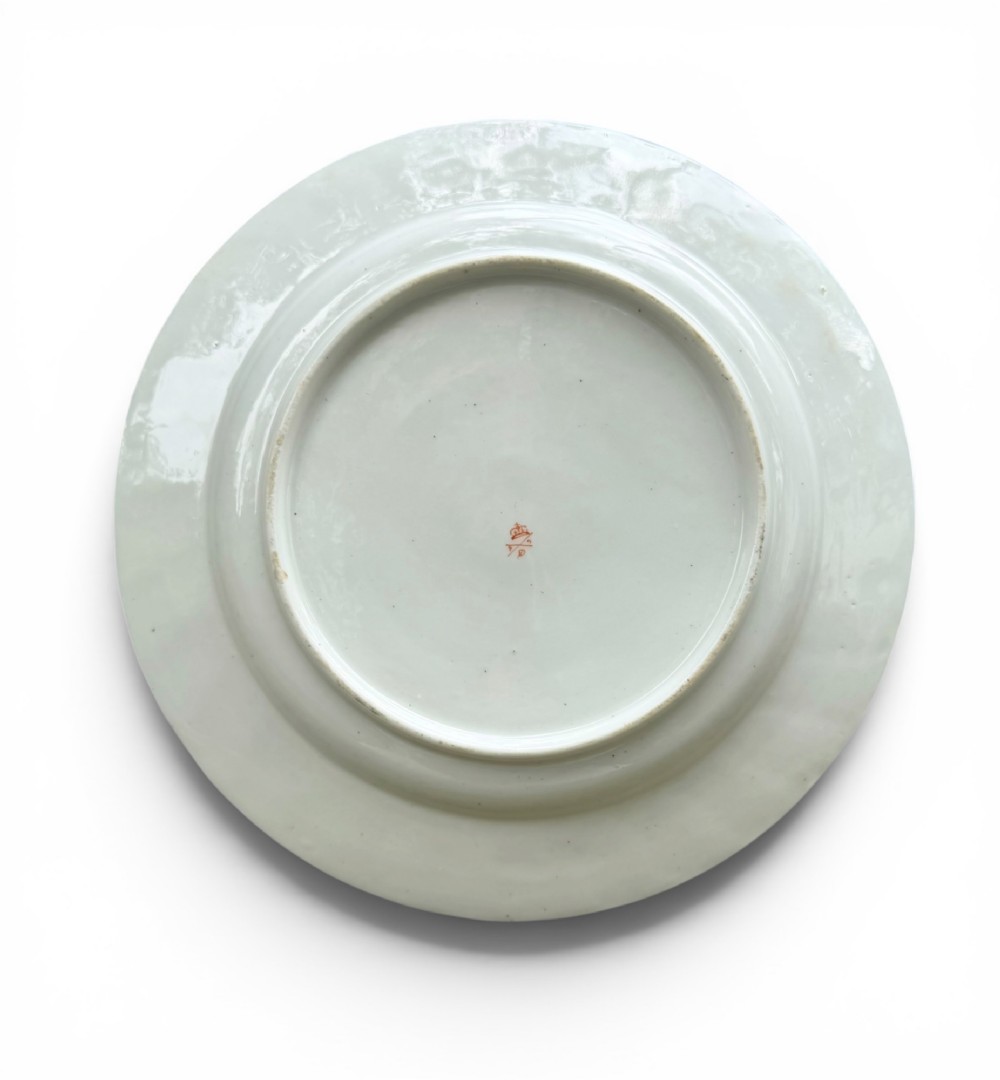 A circular white porcelain dish featuring a hand-painted floral centrepiece framed by a gilded scrollwork rim. View VI