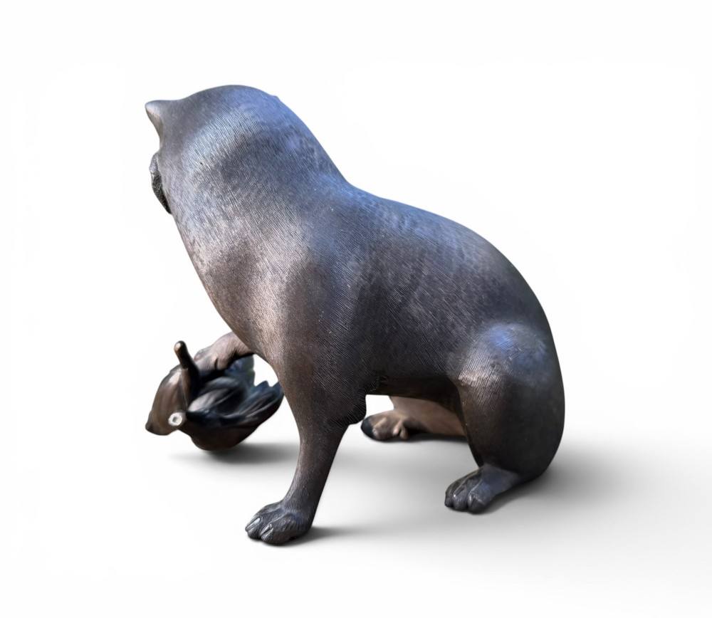 A Japanese bronze sculpture depicting a seated tanuki resting its paw on corn husks, featuring textured fur engraving and a dark patinated finish. View III