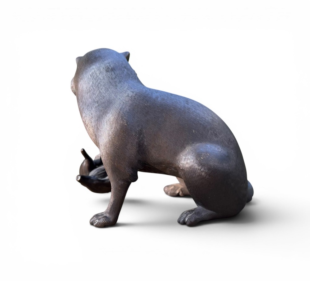 A Japanese bronze sculpture depicting a seated tanuki resting its paw on corn husks, featuring textured fur engraving and a dark patinated finish. View VII
