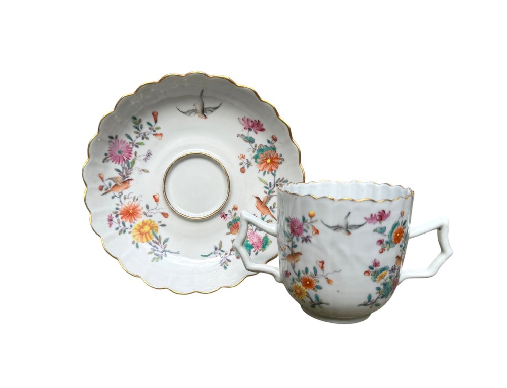A Chinese export famille rose porcelain twin-handled cup and scalloped stand decorated with hand-painted floral motifs, birds, and gilt edges.