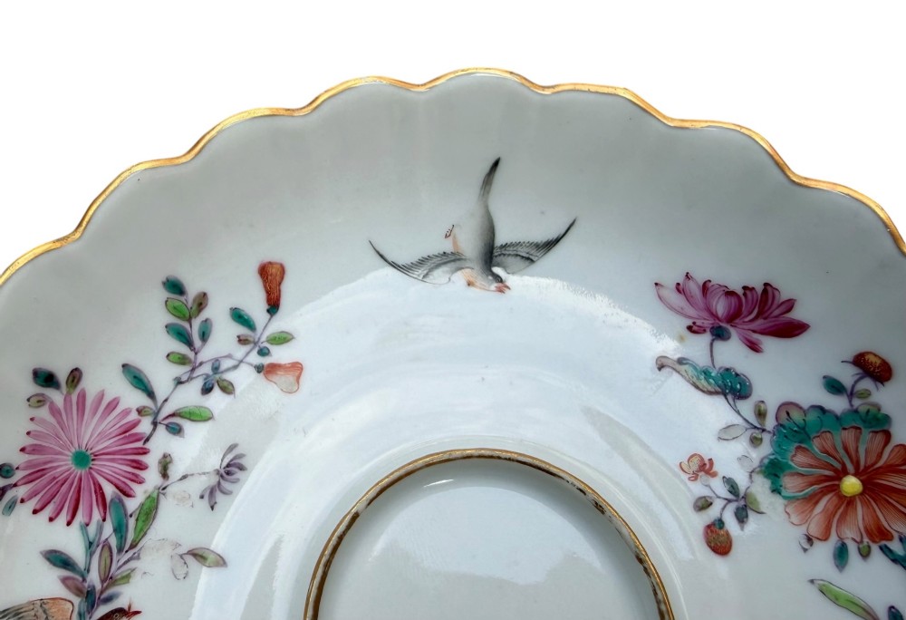 A Chinese export famille rose porcelain twin-handled cup and scalloped stand decorated with hand-painted floral motifs, birds, and gilt edges. View V