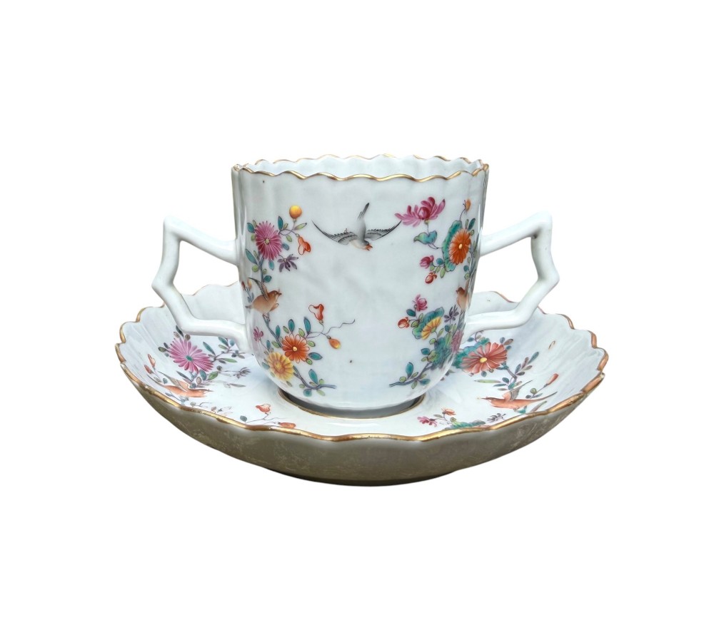 A Chinese export famille rose porcelain twin-handled cup and scalloped stand decorated with hand-painted floral motifs, birds, and gilt edges. View VI