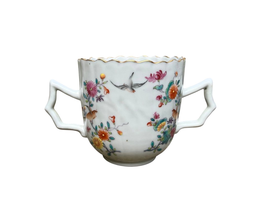A Chinese export famille rose porcelain twin-handled cup and scalloped stand decorated with hand-painted floral motifs, birds, and gilt edges. View VII