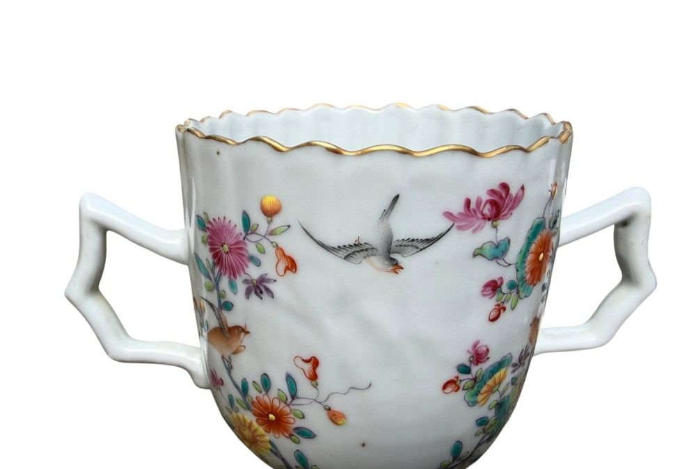 A Chinese export famille rose porcelain twin-handled cup and scalloped stand decorated with hand-painted floral motifs, birds, and gilt edges. View VIII