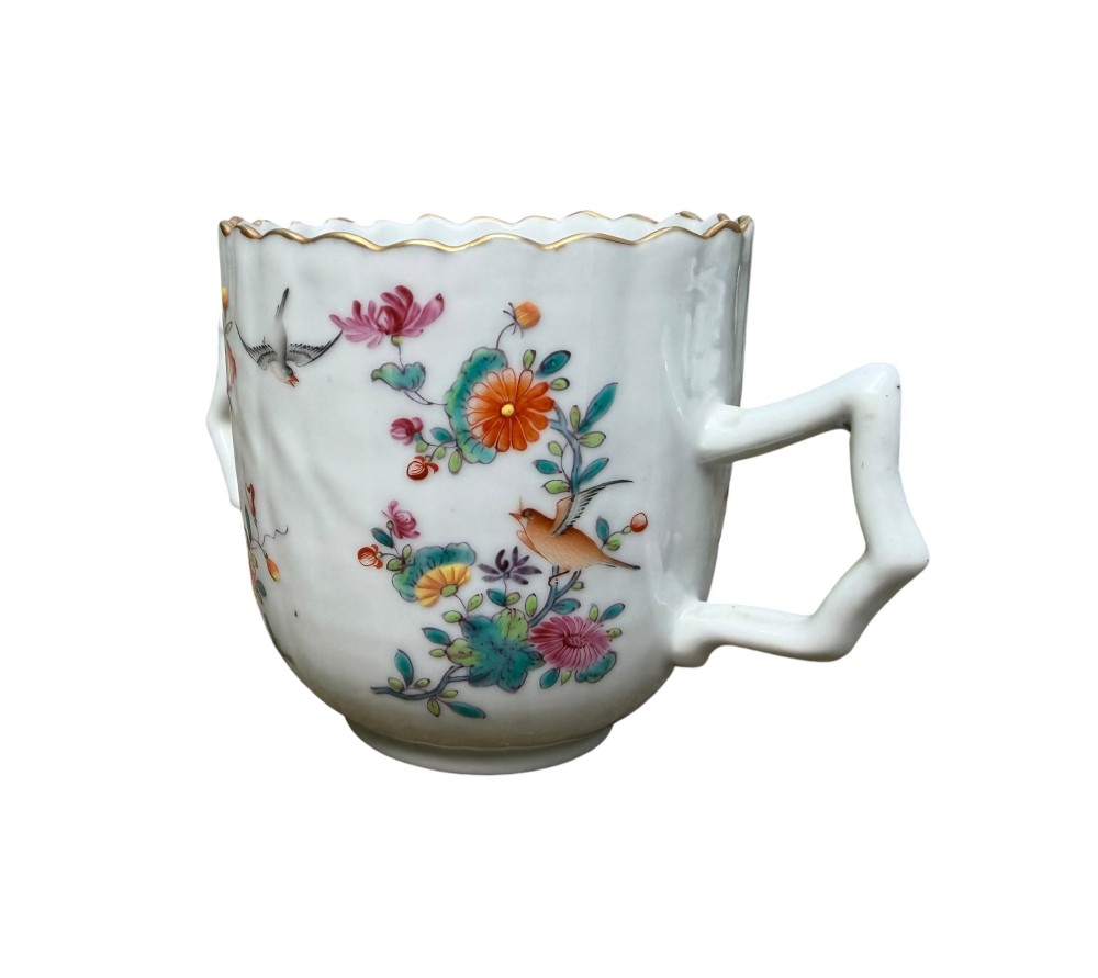 A Chinese export famille rose porcelain twin-handled cup and scalloped stand decorated with hand-painted floral motifs, birds, and gilt edges. View X