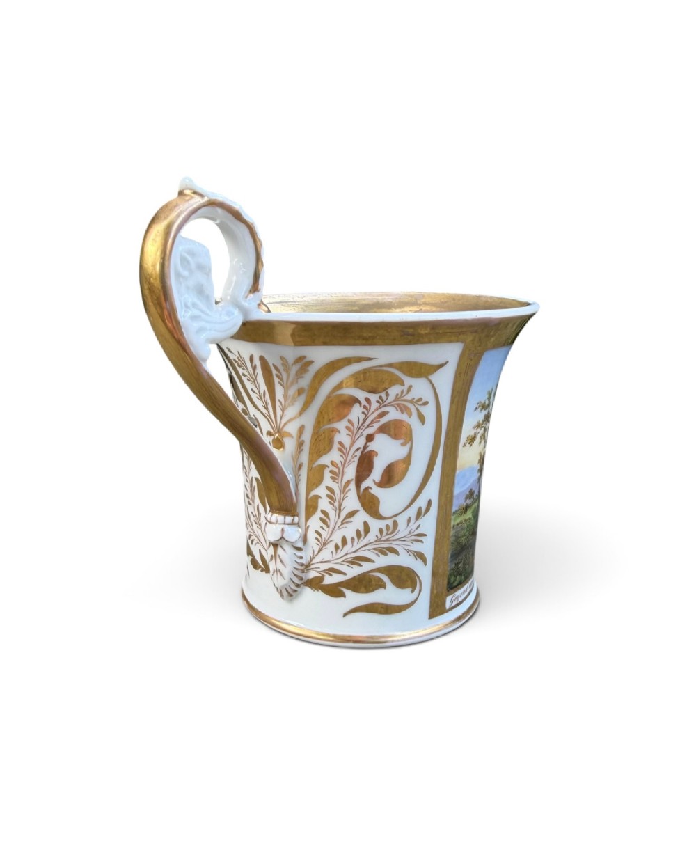An early nineteenth-century flared porcelain cabinet cup featuring a hand-painted landscape scene with a river, bridge, and hilltop ruins above inscribed German text, finished with a gilded rim and elevated handle. View III