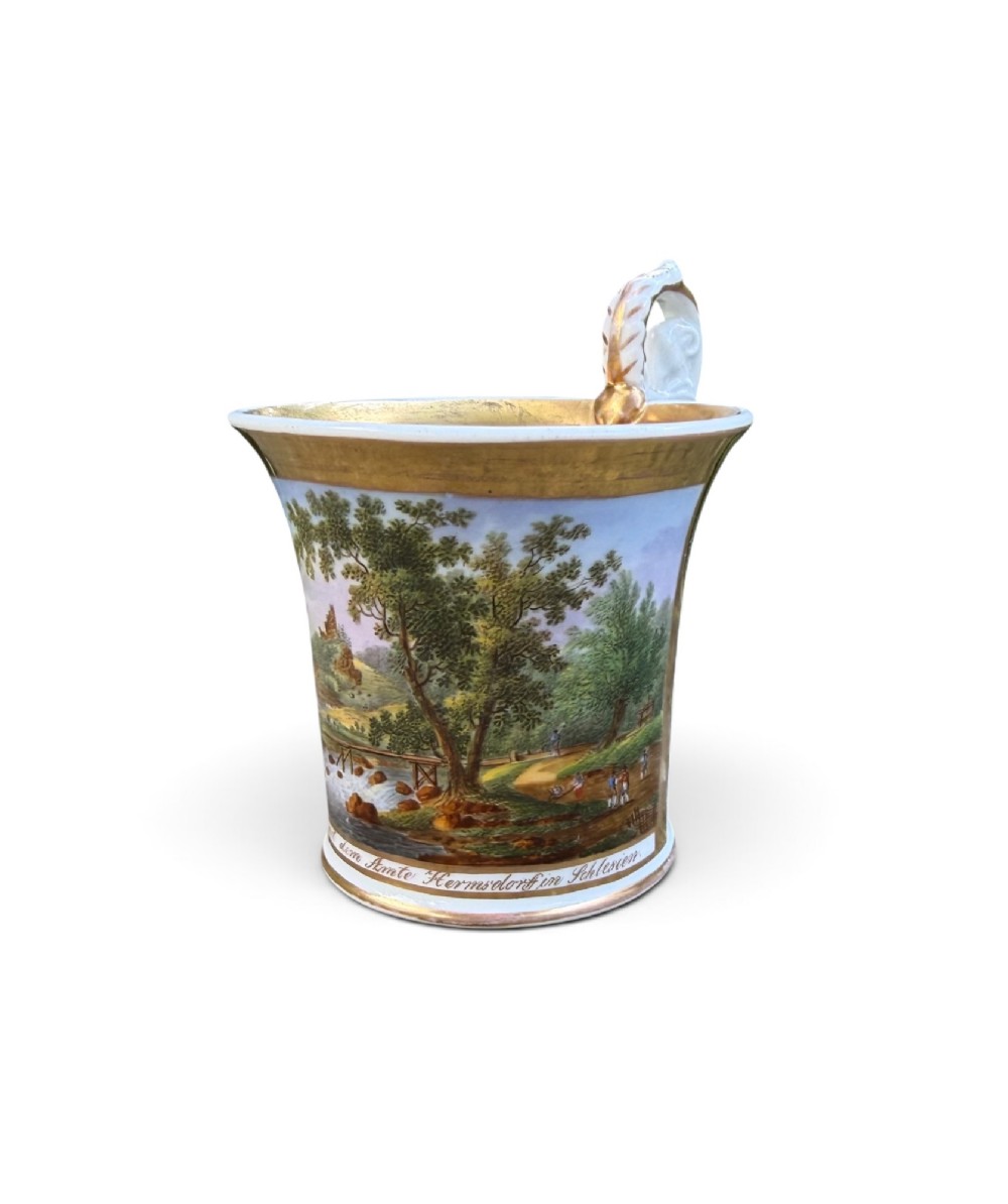 An early nineteenth-century flared porcelain cabinet cup featuring a hand-painted landscape scene with a river, bridge, and hilltop ruins above inscribed German text, finished with a gilded rim and elevated handle. View VI