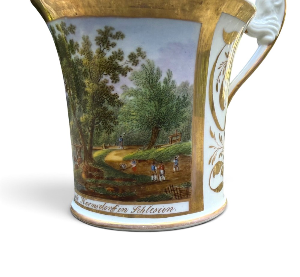 An early nineteenth-century flared porcelain cabinet cup featuring a hand-painted landscape scene with a river, bridge, and hilltop ruins above inscribed German text, finished with a gilded rim and elevated handle. View X