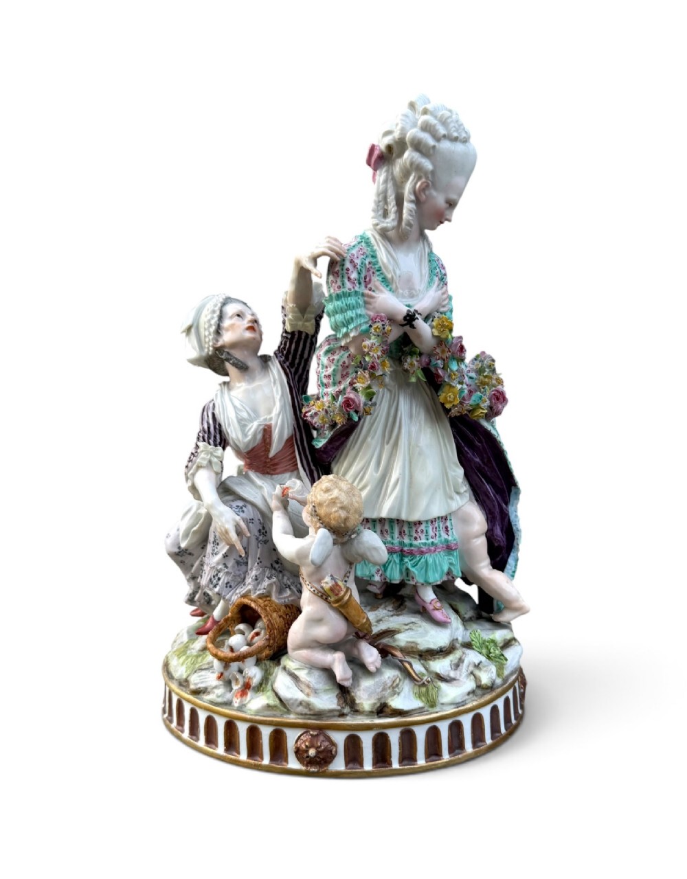 An eighteenth-century polychrome hard-paste porcelain figurine group depicting two classical figures and a cherub beside an overturned basket of eggs on a moulded fluted base.