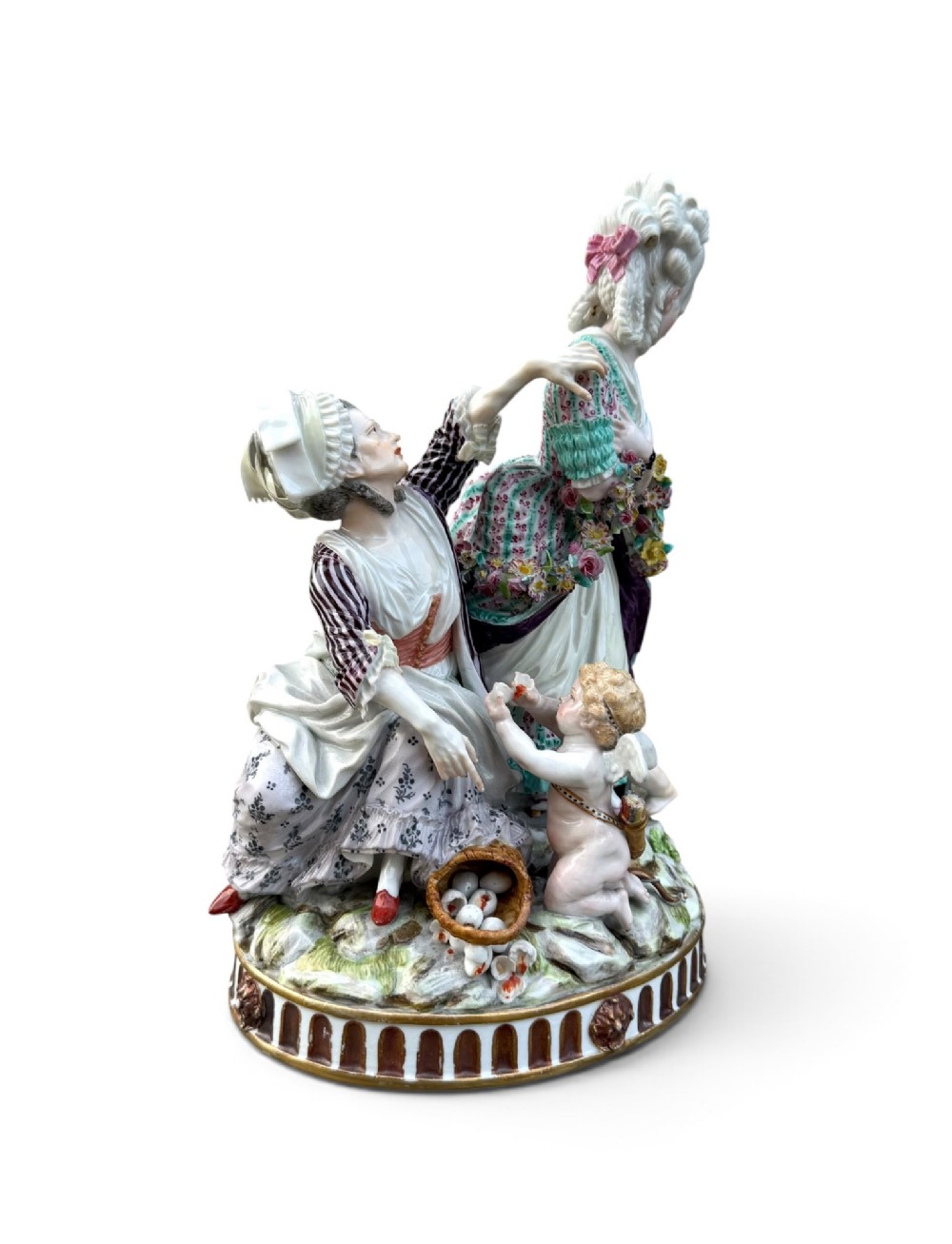 An eighteenth-century polychrome hard-paste porcelain figurine group depicting two classical figures and a cherub beside an overturned basket of eggs on a moulded fluted base. View VI