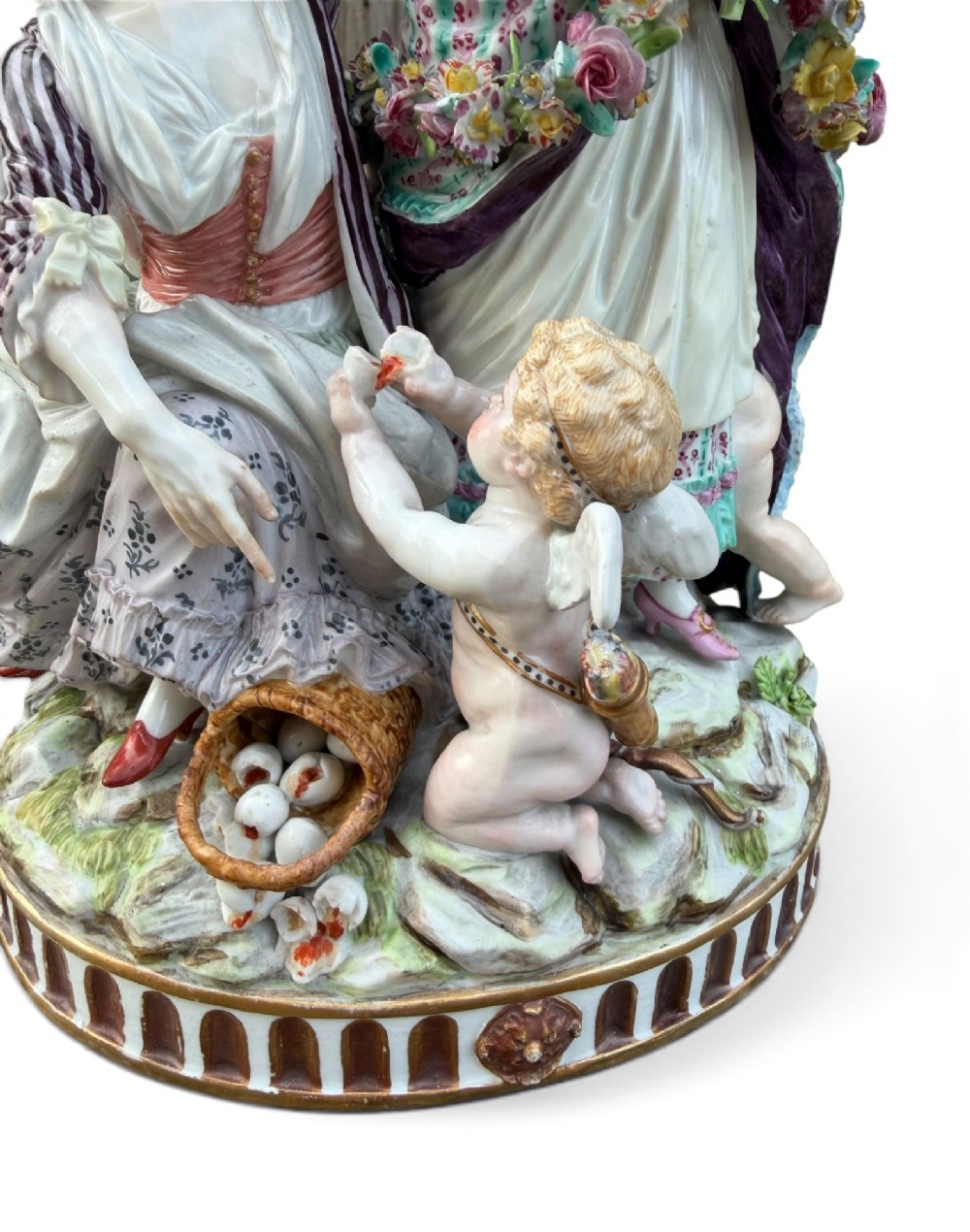 An eighteenth-century polychrome hard-paste porcelain figurine group depicting two classical figures and a cherub beside an overturned basket of eggs on a moulded fluted base. View VIII